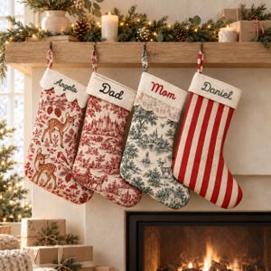 May include: Four hanging Christmas stockings with personalized names embroidered on the cuffs. The first features a red deer pattern, the second a red landscape toile, the third a green landscape toile with lace, and the fourth red stripes.
