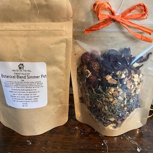 Könnte beinhalten: Zwei braune Papierbeutel mit einer botanischen Mischung für den Kochtopf. Ein Beutel hat ein weißes Etikett mit dem Text House on the Hill Forestville NY Botanical Blend Simmer Pot, Zutaten und Anweisungen. Der andere hat ein Sichtfenster mit getrockneten Pflanzen und einer orangefarbenen Schleife.