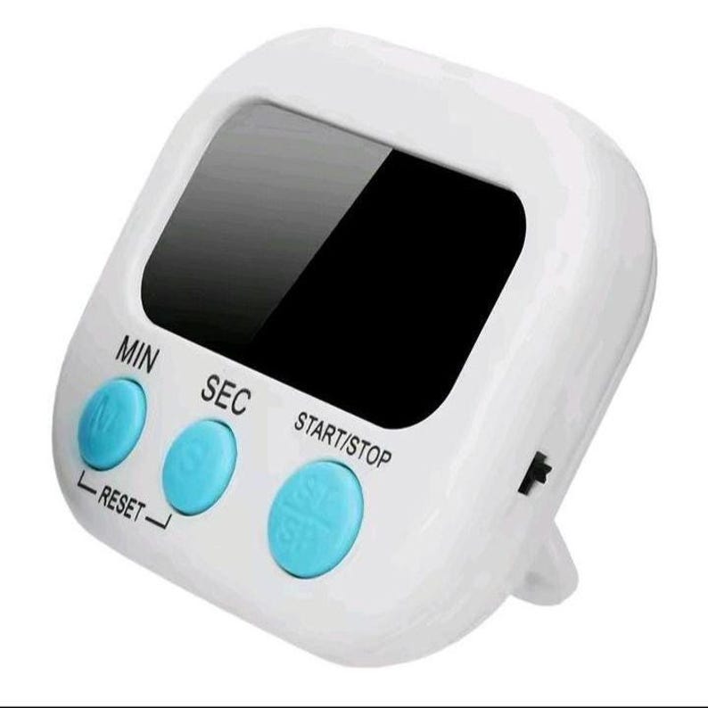 May include: A white digital kitchen timer with a black display screen and three round light blue buttons. The buttons are labeled MIN, SEC, and START/STOP, with a RESET function indicated below the first two buttons on the white plastic casing.