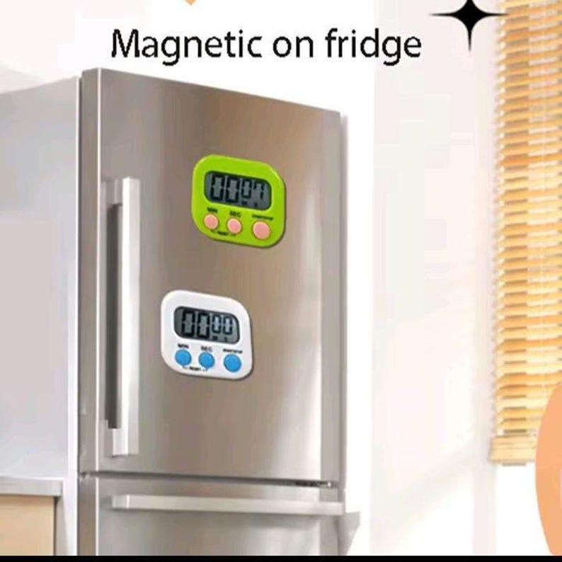 May include: Two digital kitchen timers attached to a stainless steel refrigerator. The top timer has a lime green casing with three pink buttons. The bottom timer has a white casing with three blue buttons. Both display 00:00 on their screens.