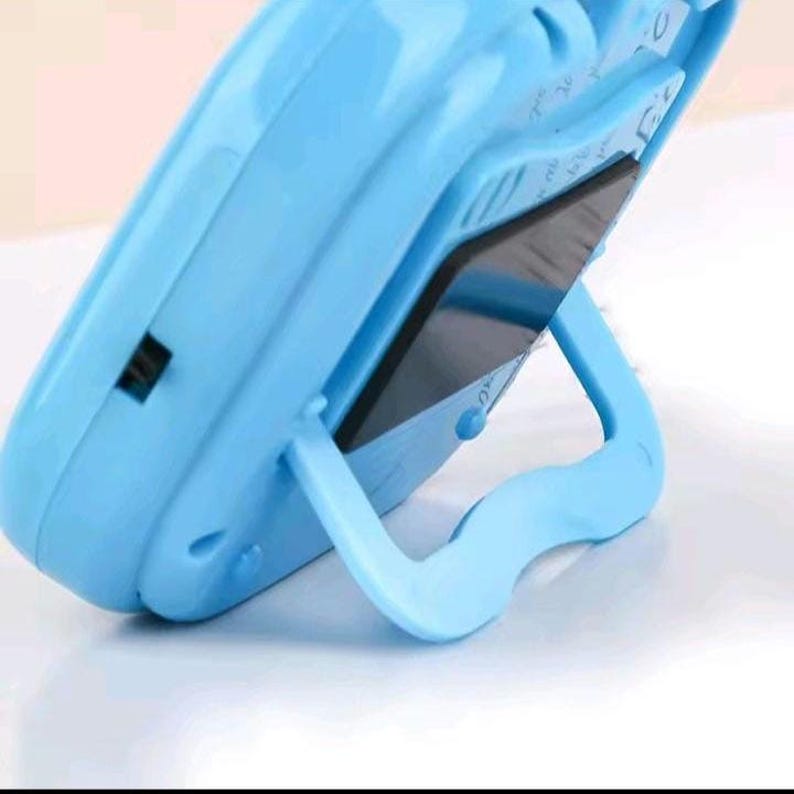 May include: A light blue plastic electronic learning device featuring a rounded, ergonomic frame and a built-in kickstand on the back. The device has a dark, reflective screen surface and a small black power switch located on the side of the casing.