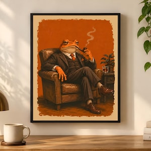 May include: A framed wall art print featuring an anthropomorphic frog dressed in a dark three-piece suit, white shirt, and orange tie. The frog sits in a brown leather armchair, holding a smoking pipe, with a glass of amber liquid on a side table.