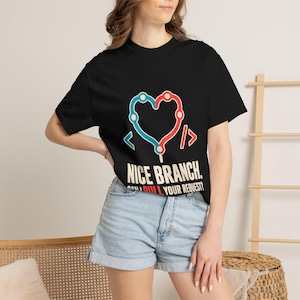 Puede incluir: Una camiseta negra de manga corta con un gráfico de un corazón formado por líneas azules y rojas con corchetes de código. El texto NICE BRANCH. CAN I PULL YOUR REQUEST? aparece en letras blancas y rojas bajo el gráfico del corazón.