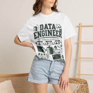 May include: A white short-sleeve t-shirt featuring a dark green graphic print that reads DATA ENGINEER and TURNING RAW DATA INTO RELIABLE PIPELINES, accompanied by a complex technical diagram of data processing icons, servers, and flow charts.