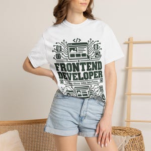 May include: A white short-sleeved t-shirt featuring a dark green graphic print of circuit board patterns, web browser icons, and the text FRONTEND DEVELOPER Turning ideas into interfaces. The design includes various coding symbols and layout elements.