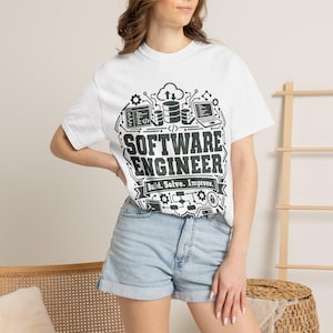 Peut inclure: Un t-shirt blanc à manches courtes avec une impression graphique noire indiquant "SOFTWARE ENGINEER" et "Build. Solve. Improve." entouré d'icônes techniques incluant des lignes de circuit, des bases de données et des écrans.