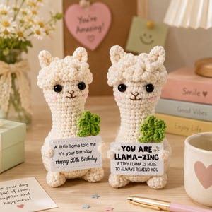May include: Two cream-colored crocheted llama figurines with black eyes and pink cheeks. Each llama holds a green crocheted four-leaf clover and a white rectangular sign. One sign reads: A little llama told me it's your birthday! Happy 30th Birthday.