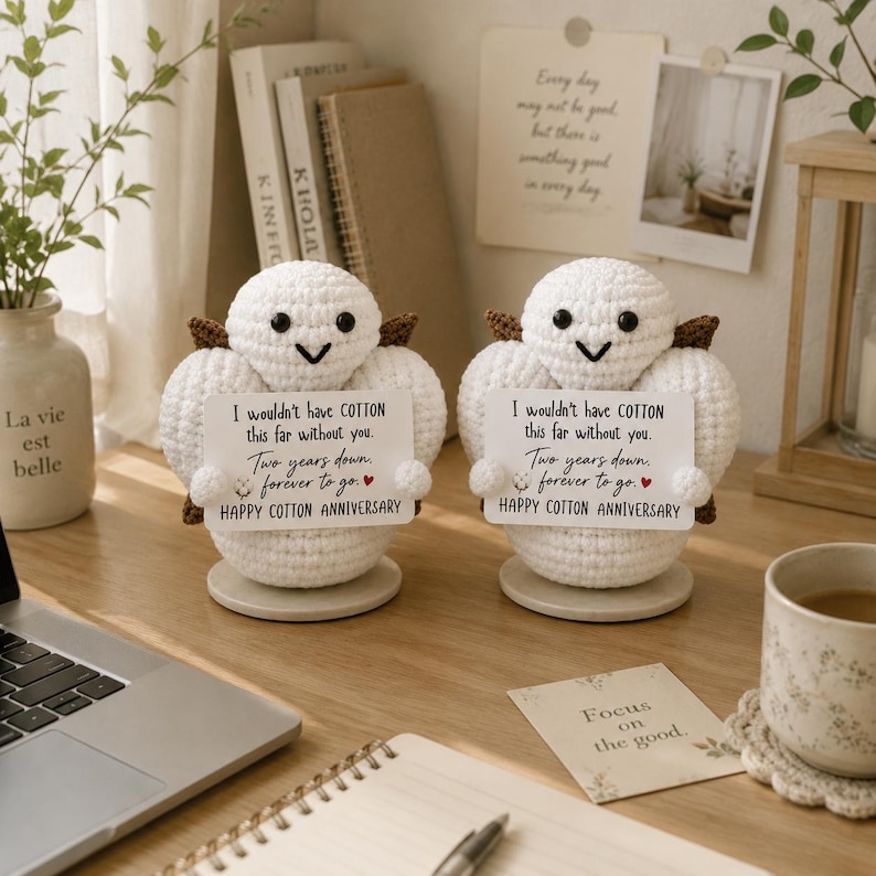 May include: Two white crocheted figures with black eyes and brown accents, each holding a card that reads: I wouldn't have COTTON this far without you. Two years down, forever to go. HAPPY COTTON ANNIVERSARY. The figures stand on circular bases.