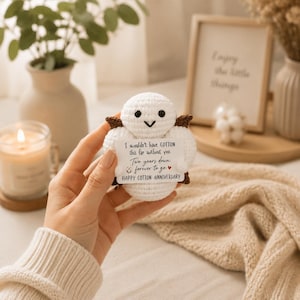 May include: A small, round, white crocheted cotton boll figure with dark brown accents, black eyes, and a V-shaped mouth. It holds a white rectangular card with the text: I wouldn't have COTTON this far without you. Two years down, forever to go. HAPPY COTTON ANNIVERSARY.