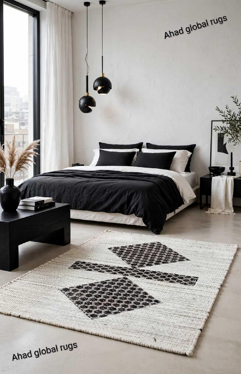 Pode incluir: Um tapete retangular com base branca e um padr&atilde;o geom&eacute;trico preto composto por duas formas de diamante ligadas por uma barra horizontal. O texto Ahad global rugs aparece nos cantos superior direito e inferior esquerdo da imagem.