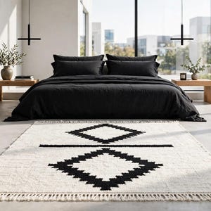 Pode incluir: Um tapete retangular com uma base de cor creme e um padr&atilde;o geom&eacute;trico preto arrojado, composto por duas formas de diamante empilhadas separadas por uma linha horizontal. O tapete tem uma textura tecida e franjas nas extremidades curtas.