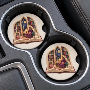 May include: Two circular car coasters featuring an illustration of an open book that forms a library scene. The scene includes a purple armchair, a lamp, a staircase, and bookshelves filled with colorful books against a night sky background.