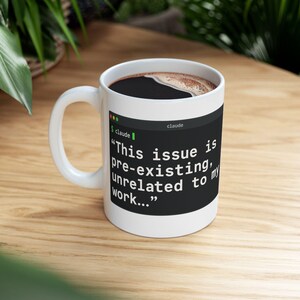 May include: A white ceramic mug featuring a black rectangular graphic resembling a computer terminal window. The text inside reads: "This issue is pre-existing, unrelated to my work..." with the word "claude" displayed at the top of the window.