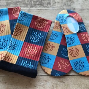 Puede incluir: Un par de calcetines con un patrón a cuadros que presenta una imagen repetida de fresas en rojo, azul, amarillo y marrón. Un calcetín es un calcetín de deporte y el otro es un calcetín invisible.