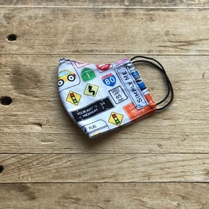May include: A white face mask with a road sign pattern. The mask has black elastic ear loops and features road signs with text like "Speed Limit 65", "Your Way 3/4", "Highway 2", and "Simply Me".