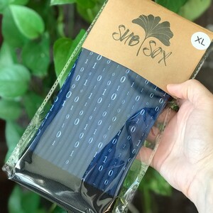 K&ouml;nnte beinhalten: Ein Paar blaue Socken mit einem wei&szlig;en Bin&auml;rcode-Muster. Die Socken sind in einer durchsichtigen Plastikt&uuml;te verpackt, die mit einem braunen Papieretikett mit der Aufschrift "SUB SOX" und "XL" versehen ist.