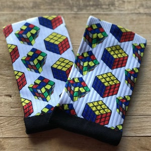 Może przedstawiać: Para białych skarpet z kolorowym wzorem kostki Rubika. Skarpety mają czarne mankiety.