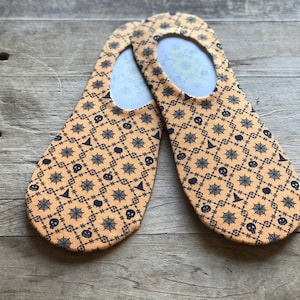 Puede incluir: Un par de calcetines invisibles de color naranja y negro con un patrón de temática de Halloween. El patrón presenta un diseño repetitivo de telarañas, calaveras, calabazas y sombreros de bruja.