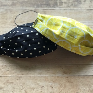 May include: Two fabric face masks, one black with white polka dots and one yellow with white lemon slices.