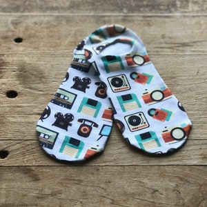 Puede incluir: Un par de calcetines blancos hasta el tobillo con un estampado de temática retro que presenta imágenes de cintas de cassette, disquetes, cámaras y tocadiscos.