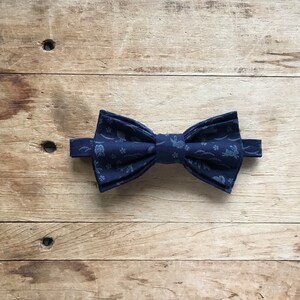 May include: A navy blue bow tie with a white pattern of rabbits and flowers.