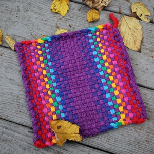 May include: A square, woven potholder with a rainbow gradient design. The potholder transitions from red to purple, with a rainbow stripe along one side. A red loop is attached for hanging. The potholder is approximately 20 cm square.
