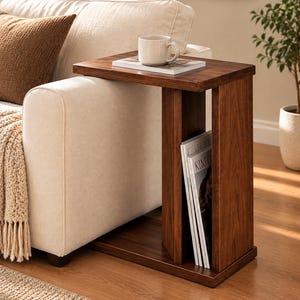May include: A rectangular dark wood C-shaped side table with a flat top surface and a vertical storage compartment. The table features a smooth finish and a hollow center section designed to hold magazines or books upright in a vertical stack.