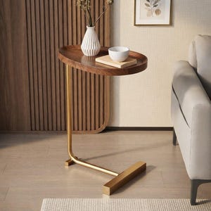 May include: A C-shaped side table featuring a dark brown wooden oval tabletop with a raised edge and a gold-toned metal frame. The base consists of a horizontal bar that supports the vertical stand, which connects to the underside of the tabletop.