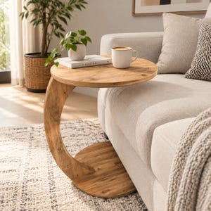 May include: A C-shaped side table crafted from light brown wood with a circular top and a matching circular base. The table features a curved support column connecting the top and bottom, providing a stable structure for holding items.