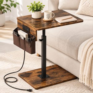 May include: A C-shaped side table with a rustic brown wood-grain finish, a black metal frame, and an adjustable height post. It features a built-in power outlet with two sockets and a brown fabric storage pocket containing books and pens.