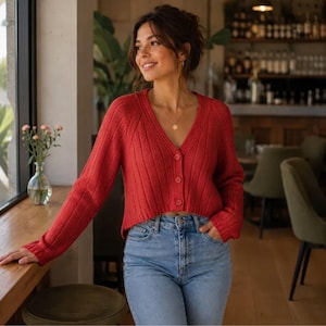 May include: A vibrant red, long-sleeved, ribbed knit cardigan featuring a V-neckline and three matching buttons down the front, paired with light blue denim jeans. The cardigan has a cropped length and a textured, vertical ribbed pattern.