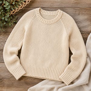 Könnte beinhalten: Ein cremefarbener Langarmpullover mit klassischem Rundhalsausschnitt, Raglanärmeln und einer gerippten Strickstruktur an Kragen, Bündchen und Saum. Das Kleidungsstück ist durchgehend mit einem gleichmäßigen Strickmuster am Körper und an den Ärmeln gefertigt.