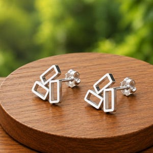 May include: A pair of silver stud earrings, each featuring three interconnected rectangular frames arranged in a cluster. The earrings have a polished metallic finish and include standard post backs for secure attachment to the earlobe.