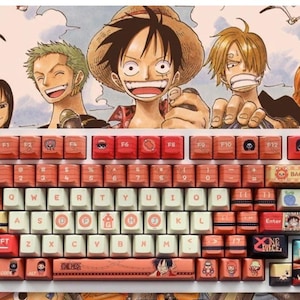 以下が含まれることがあります： アニメ「ONE PIECE」をテーマにしたカスタムキーキャップセット付きのメカニカルキーボード。トップパネルにはルフィ、ゾロ、サンジのイラストが描かれています。キーはクリーム色と赤の組み合わせで、様々なキャラクターアイコンと「ONE PIECE」の文字が印字されています。