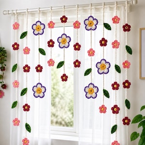 Puede incluir: Una cortina de ventana con múltiples hilos de ganchillo verticales que cuelgan de una barra. Cada hilo está decorado con varias flores de ganchillo en tonos morado, blanco, amarillo, rosa y rojo oscuro, intercaladas con pequeñas hojas verdes.