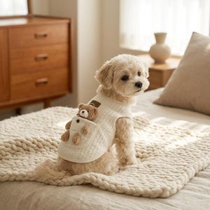 Peut inclure: Un gilet pour chien matelassé de couleur crème avec un petit ours en peluche marron fixé sur une poche avant. Le gilet est sans manches, doté d'une encolure ronde simple et d'un petit écusson rectangulaire près du col, conçu pour les chiens.