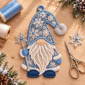 May include: A blue and white embroidered gnome ornament featuring a snowflake pattern, a long beard, and a matching hat with a pom-pom. The gnome holds a snowflake-shaped wand, accented with small blue beads and intricate lace-like stitching.