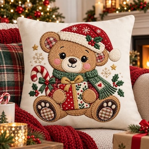 May include: A square off-white throw pillow featuring an embroidered brown teddy bear wearing a red Santa hat with white trim and holly. The bear holds a candy cane and a gift box, wearing a green scarf with a heart patch, surrounded by snowflakes.