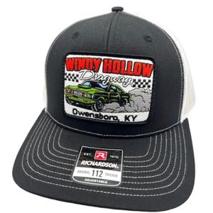 May include: A black and white trucker cap featuring a rectangular patch with a green car graphic, the text Windy Hollow Dragway, and Owensboro, KY. The front panel is black with white stitching, and a Richardson 112 adjustable sticker is on the brim.