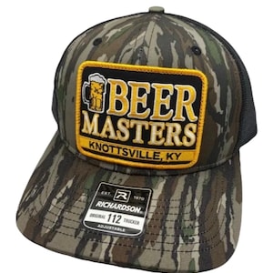 May include: A camouflage trucker hat with a black mesh back and a rectangular patch on the front. The patch features a beer mug icon, the text BEER MASTERS, and KNOTTSVILLE, KY. A black Richardson 112 sticker is on the brim of the hat.
