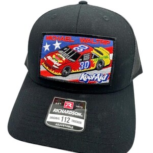 May include: A black trucker hat featuring a rectangular embroidered patch of a red race car with the number 30 and the text Michael Waltrip and Kool-Aid. A black sticker on the brim displays the text Richardson Est. 1970 Original 112 Trucker Adjustable.