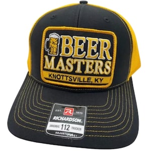 May include: A black and yellow trucker cap featuring a rectangular patch with a beer mug graphic and the text BEER MASTERS KNOTTSVILLE, KY. The front panel is black with yellow stitching, and a Richardson 112 adjustable sticker is on the brim.