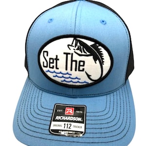 May include: A light blue trucker cap with a black mesh back and black brim stitching. The front features an oval patch with the text Set The, a black fish graphic, and blue wave lines. A black Richardson 112 Original adjustable sticker is attached.