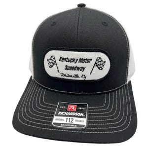 Peut inclure: Une casquette de type trucker noire et blanche avec un écusson rectangulaire blanc portant le texte noir Kentucky Motor Speedway Whitesville, KY et deux drapeaux à damier. La visière présente des surpiqûres blanches et un autocollant noir.