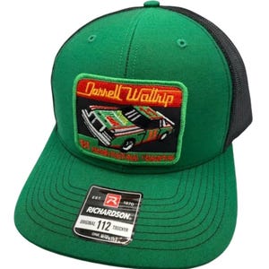 May include: A green and black trucker hat featuring a rectangular patch with an embroidered race car and the text Darrell Waltrip 81 Grand National Champion. A black Richardson 112 Original Trucker sticker is affixed to the green brim.