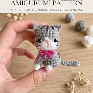 May include: A small gray and white crocheted cat amigurumi with black embroidered whiskers, black eyes, a pink nose, and a bright pink bow around its neck. The text MINI CAT AMIGURUMI PATTERN and Digital Pattern | Step-by-Step Guide are visible.