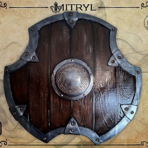 Könnte beinhalten: Ein hölzerner Schild mit dunkelbraunem Finish, akzentuiert durch einen silberfarbenen Metallrahmen und einem zentralen kreisförmigen Emblem. Der Schild hat ein verwittertes Aussehen, mit sichtbarer Holzmaserung und Metallnieten. Das Wort "MITRYL" steht oben.
