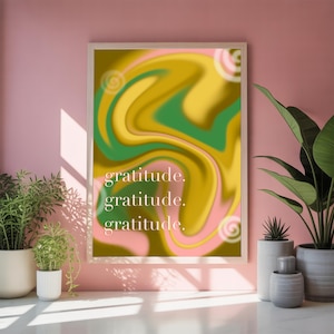 May include: A rectangular wall art print in a light wood frame featuring a swirling abstract pattern of mustard yellow, forest green, and soft pink. The word gratitude is printed in white lowercase letters three times in the center.