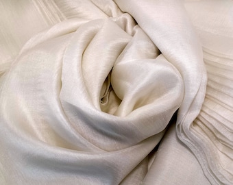 May include: A close-up of a white fabric with a silky texture. The fabric is folded and draped in a way that creates a soft, flowing look.