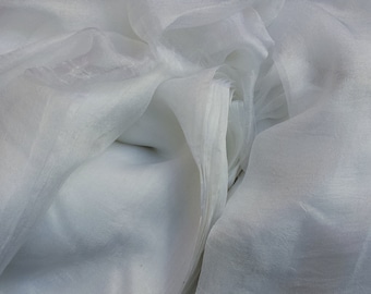 May include: A close-up of white sheer fabric, with soft folds and a translucent appearance. The fabric is layered, creating depth and texture. The material appears lightweight and delicate, suitable for drapery or apparel.